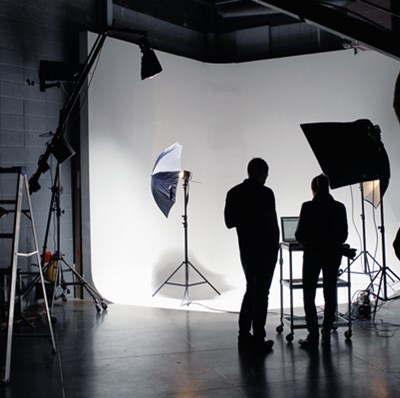 Silhouettes of four people in a studio working around a white screen with a photography reflective umbrellas