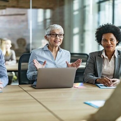 A man, women with a laptop open in front of her and another women sitting in a row facing a women we have a back view of A man, women with a laptop open in front of her and another women sitting in a row facing a women we have a back view of
