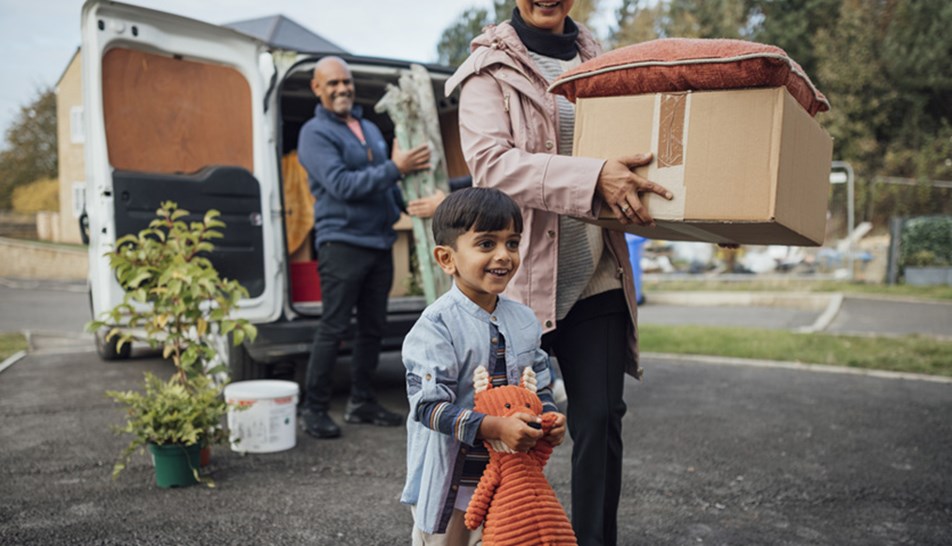 Couple carrying boxes from removal van with small child in the foreground