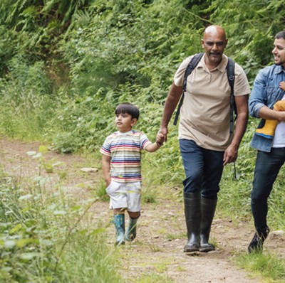 Grandfather holding hands with grandson and father carrying his daughter while walking along a dirt track lined with greenery Grandfather holding hands with grandson and father carrying his daughter while walking along a dirt track lined with greenery