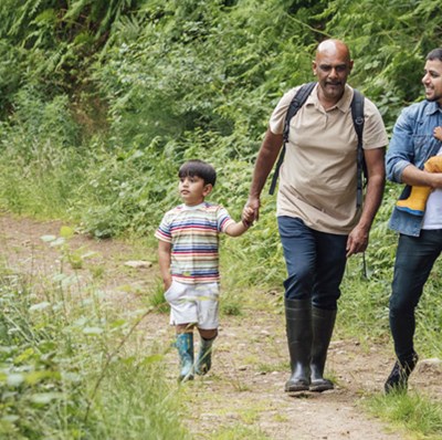 Grandfather holding hands with grandson and father carrying his daughter while walking along a dirt track lined with greenery