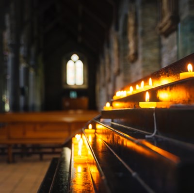 Shelf of prayer candle votives in a church with a view of pews, church pillars and windows