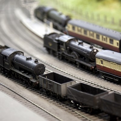 Four curving tracks of a model railway with two steam trains and their coaches and one with open topped goods wagons Four curving tracks of a model railway with two steam trains and their coaches and one with open topped goods wagons