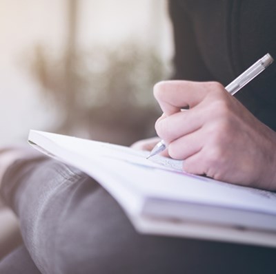 Man with their leg at a right angle across their knee being using it to write on an A4 note pad