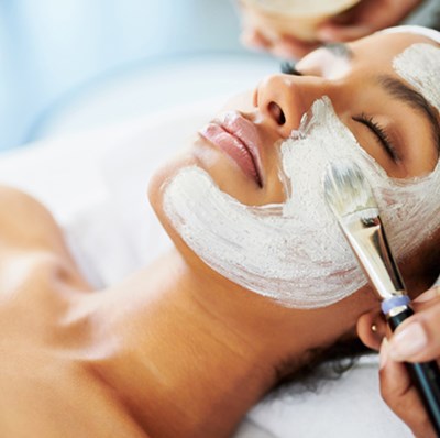 A woman wearing a towel, lying down, with her hair covered, having a paste brushed onto her face A woman wearing a towel, lying down, with her hair covered, having a paste brushed onto her face
