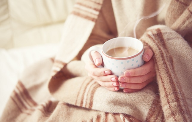 Person wrapped in blanket holding steaming cup of tea