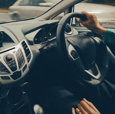 Passenger view of a drivers hands on a steering wheel on a road lined with trees Passenger view of a drivers hands on a steering wheel on a road lined with trees