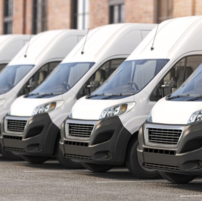 Row of parked white vans with blurred backdrop of buildings  Row of parked white vans with blurred backdrop of buildings