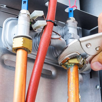 Hand view of a wrench being use on a nut for a copper tube on the back of a rectangle metal  box with two other tubes Hand view of a wrench being use on a nut for a copper tube on the back of a rectangle metal  box with two other tubes