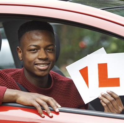 Young male learner sat in red car holding L plates Young male learner sat in red car holding L plates