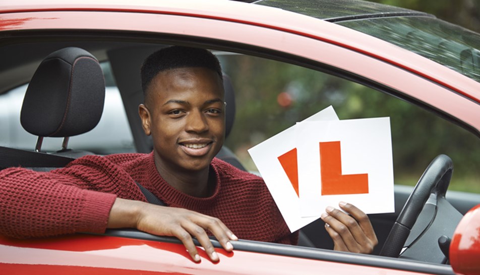 Young male learner sat in red car holding L plates