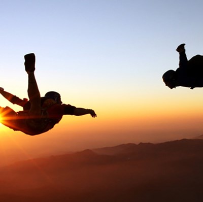 Couple skydiving with a sunset background and dusky mountaintops
