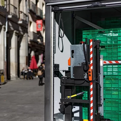 Green plastic food crates stacked in a van with a roller shutter door, a street view to the left hand side of stone buildings on a wide footpath