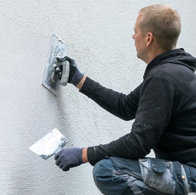 Young man plastering a textured surface on an exterior wall Young man plastering a textured surface on an exterior wall